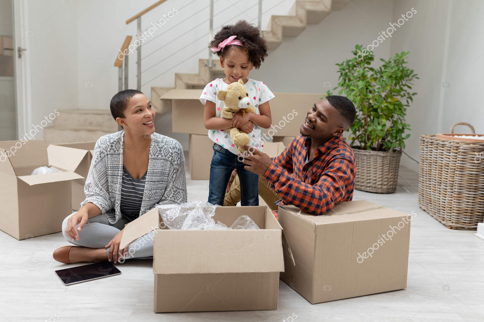 Front view of happy African american family unpacking cardboard boxes in living room at home